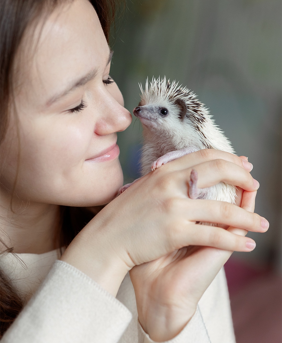 A young woman holding her hedgehog up to face while smiling